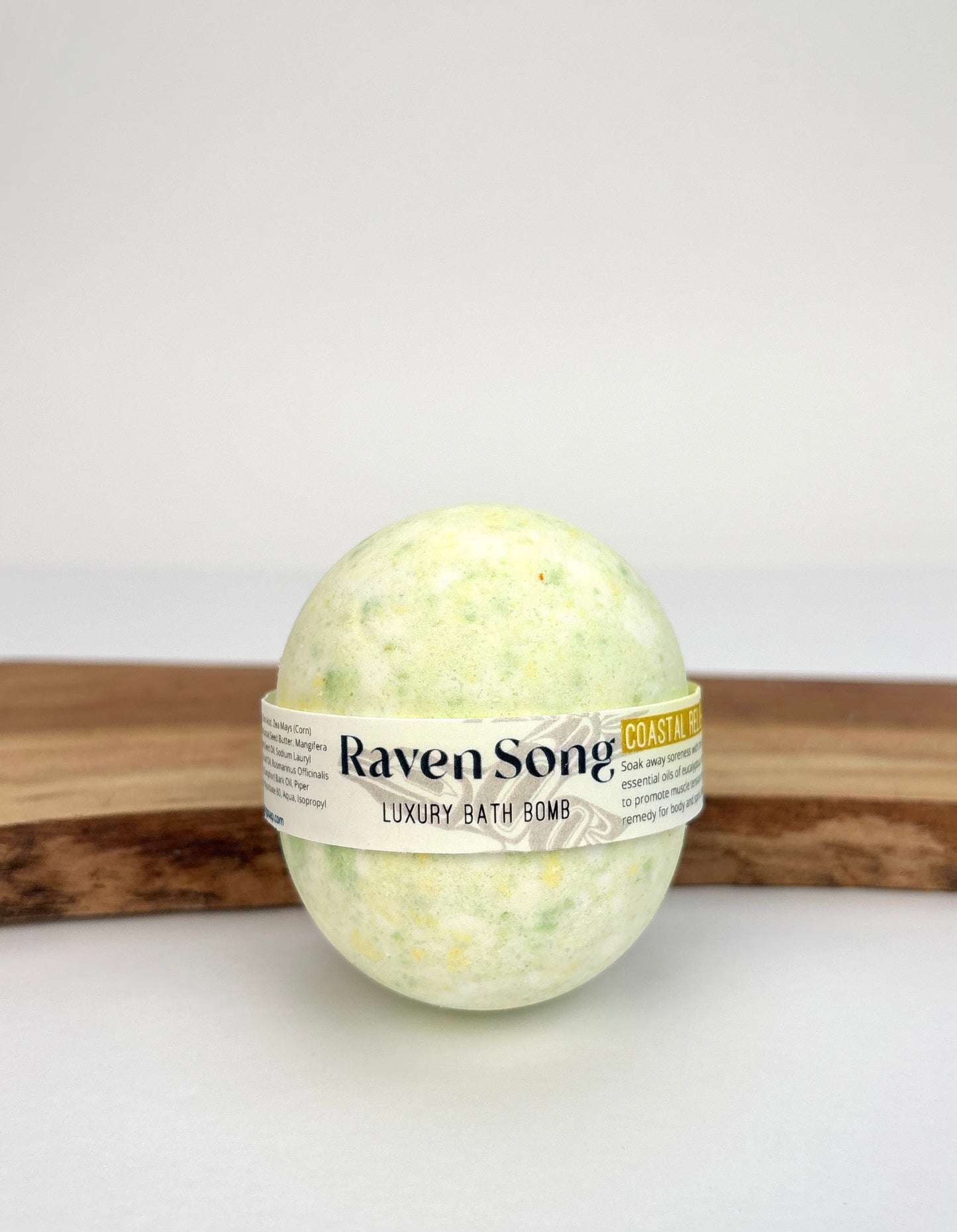 RavenSong Coastal Relief bath bomb in pale green, wrapped in a Luxury Bath Bomb label and resting on a wooden stand