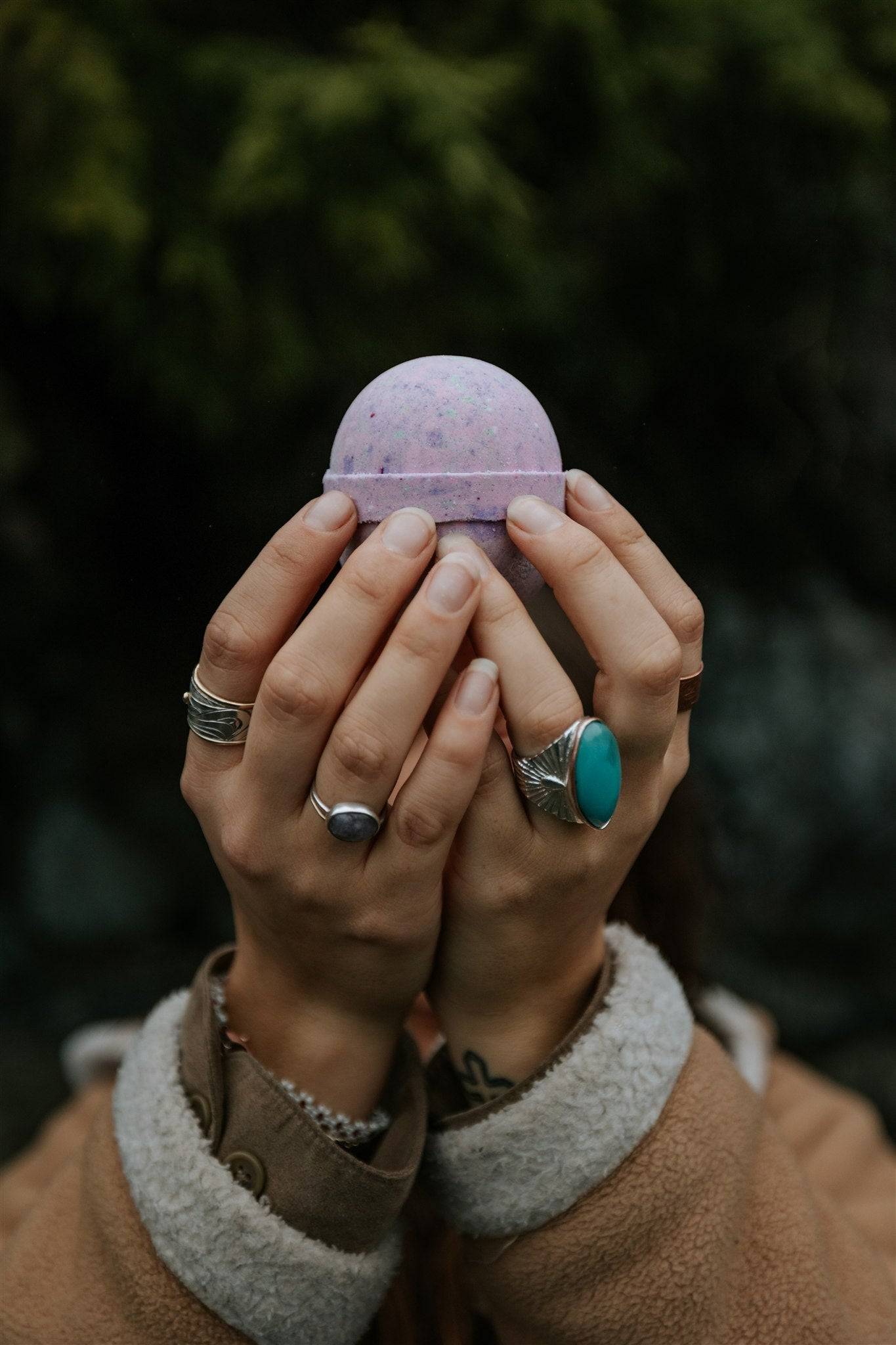 Person holding a pink bath bomb with greenery in the background