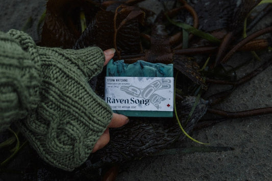 Storm Watching soap by RavenSong in its wrapped label showing net weight 115 g, held above beach kelp