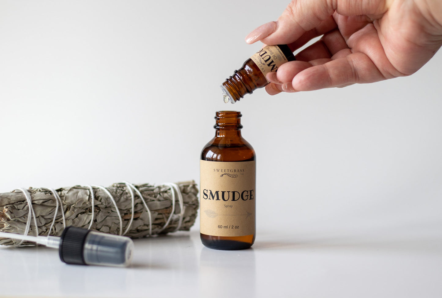 Smudge Oil Blend being dripped into a Smudge Spray bottle to top it up, sage bundle beside.