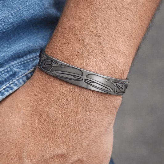 Silver bracelet with tribal design on a wrist against a blurred background