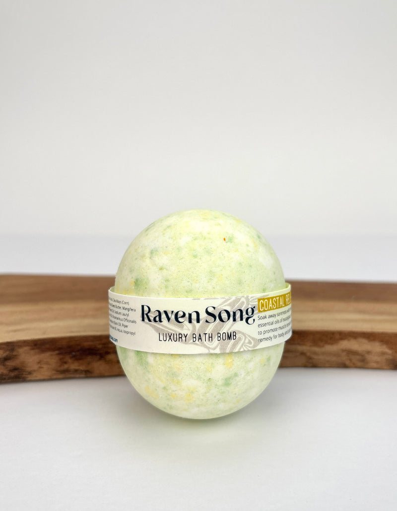 RavenSong Coastal Relief bath bomb in pale green, wrapped in a Luxury Bath Bomb label and resting on a wooden stand