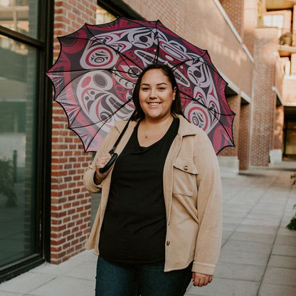 Lady standing on a sidewalk in front of a building holding the Pacific Umbrella Thunder Moon by Indigenous Artist Joe Wilson-Sxwaset