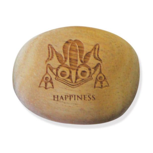 Photo of Frog Indigenous Design by Ernest  Swanson carved into a small wooden stone / rock with the word happiness engraved into the stone. It is displayed in front of a white background