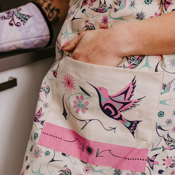 Person wearing a floral-patterned garment with a close-up of a pocket featuring a hummingbird design.
