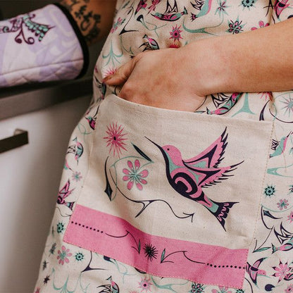 Person wearing a floral-patterned garment with a close-up of a pocket featuring a hummingbird design.