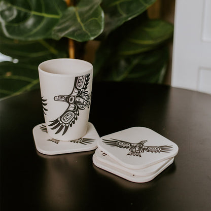 Bamboo eagle coasters stacked and a bamboo cup resting on one of the coasters. Displayed on a black table