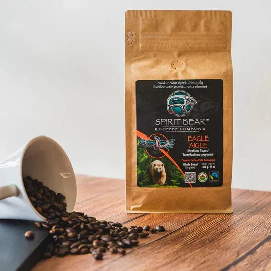 Coffee bag from Spirit Bear Coffee Company with coffee beans spilling out on a wooden surface.
