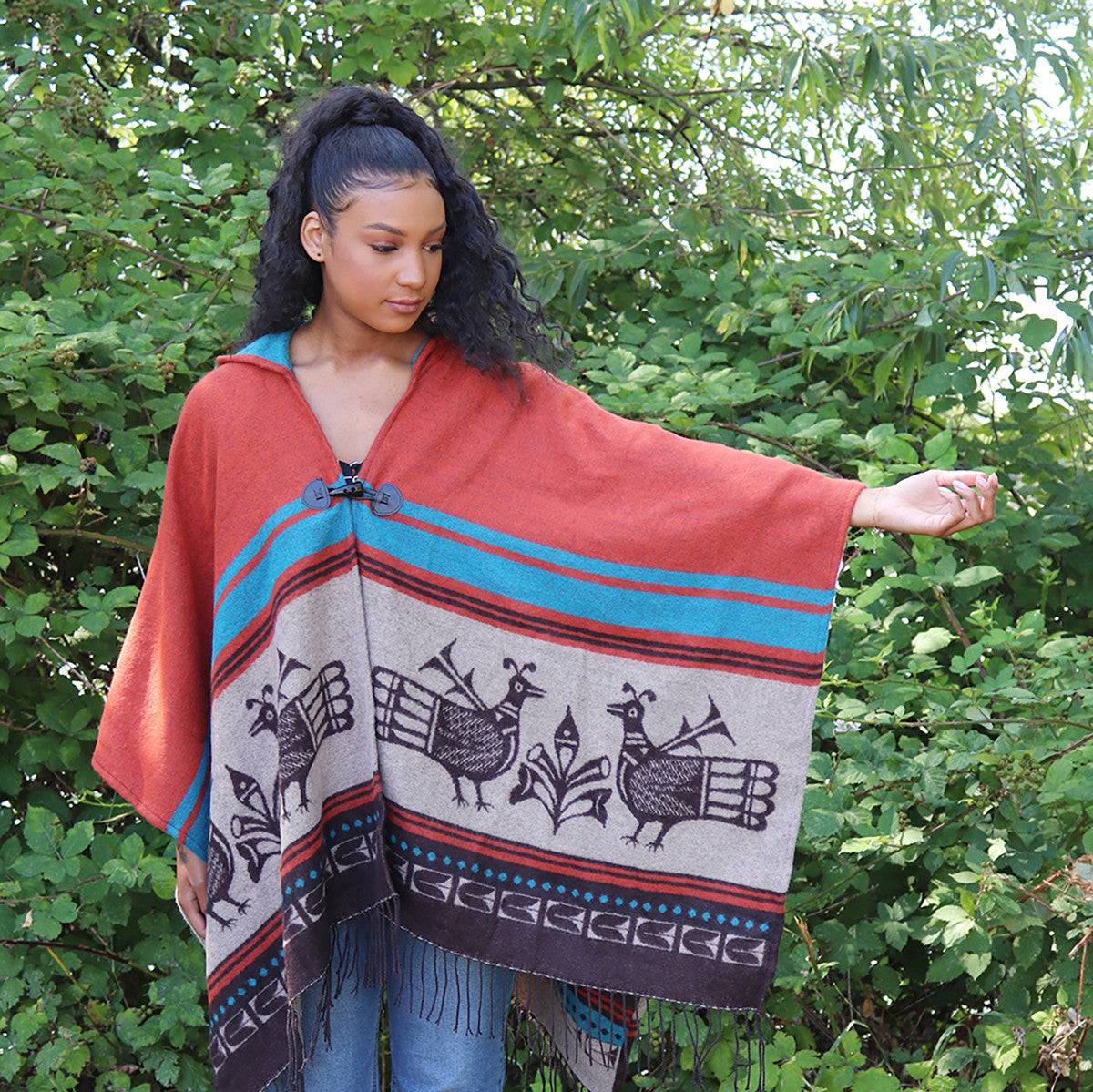 Woman wearing a red and patterned poncho in front of green foliage