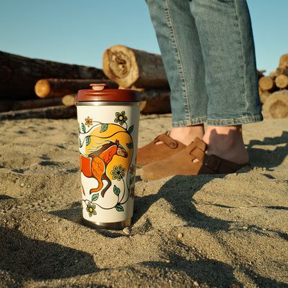 Person standing on a sandy beach with a decorated cup and wooden logs in the background