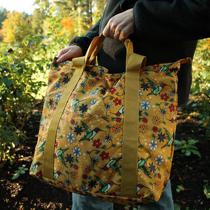 Person holding a yellow floral-patterned bag in an outdoor setting with greenery.
