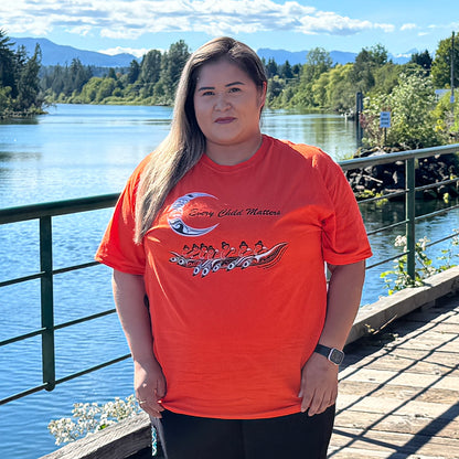Person wearing the orange Every Child Matters t-shirt with The Children Are Coming Home design, standing by the water