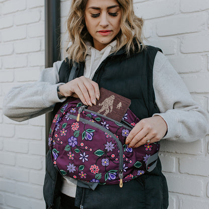 Ojibwe Florals sling pack worn at the front, hand reaching into the zip pocket