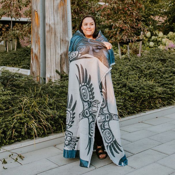 Woman standing in nature with the Soaring Eagle woven blanket wrapped around her body 