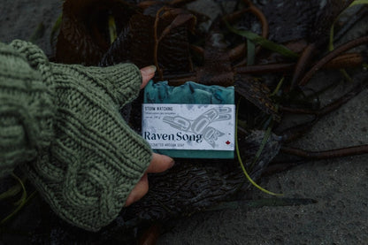 Storm Watching soap by RavenSong in its wrapped label showing net weight 115 g, held above beach kelp