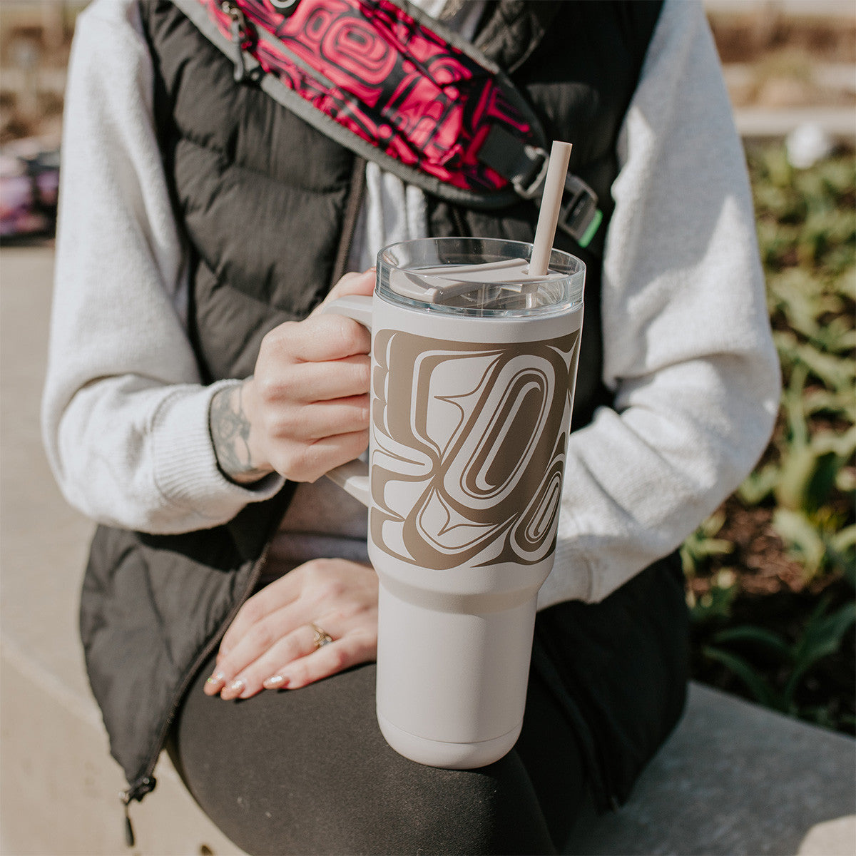 Person holding a white tumbler with a Indigenous eagle design outdoors