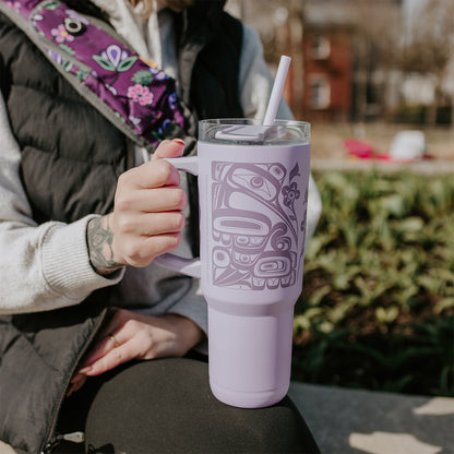 Person holding a purple tumbler with a design outdoors.