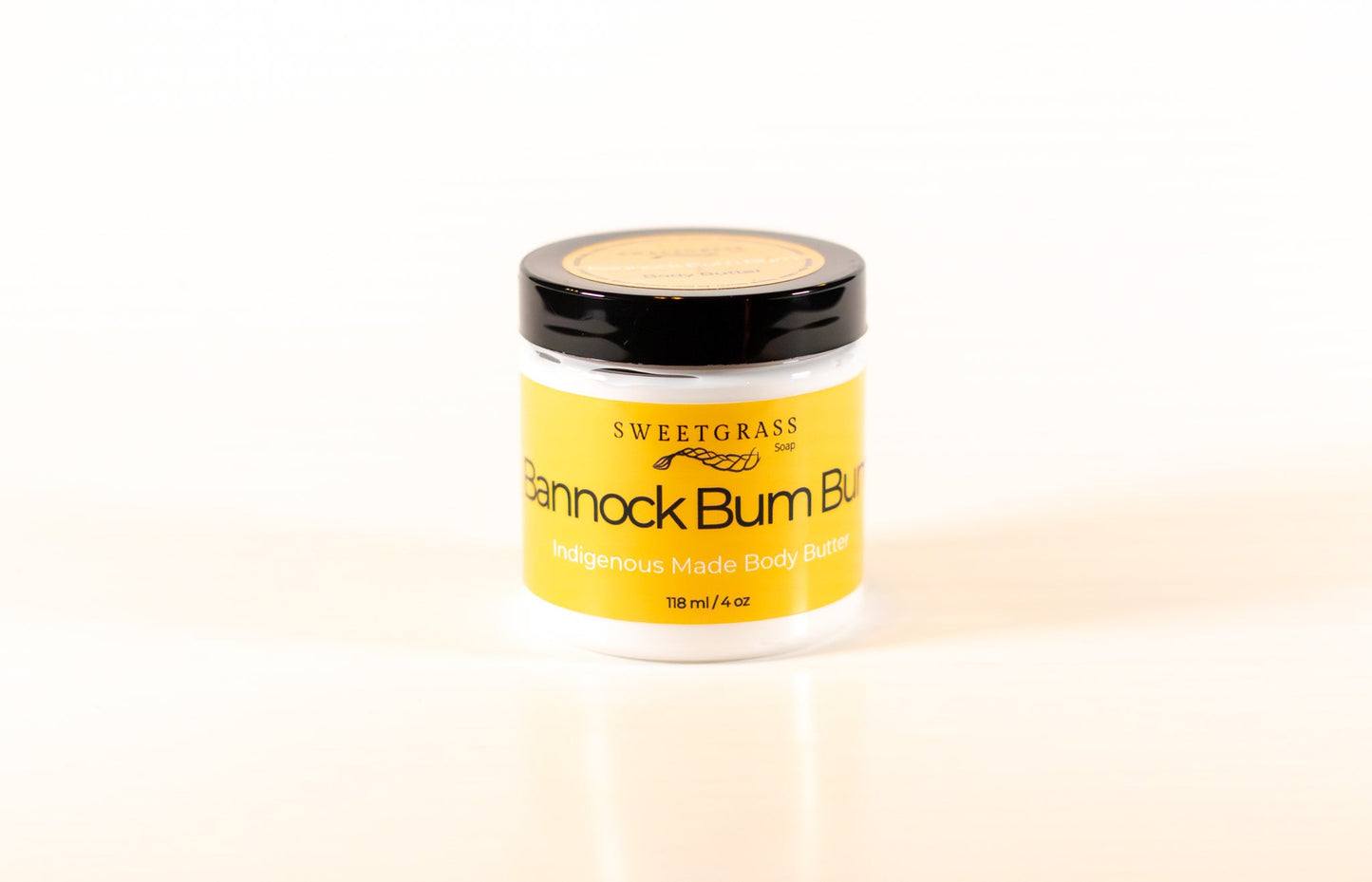 Sweetgrass Soap Bannock Bum Bum body butter in a clear jar with a black lid and yellow label, 118 ml.