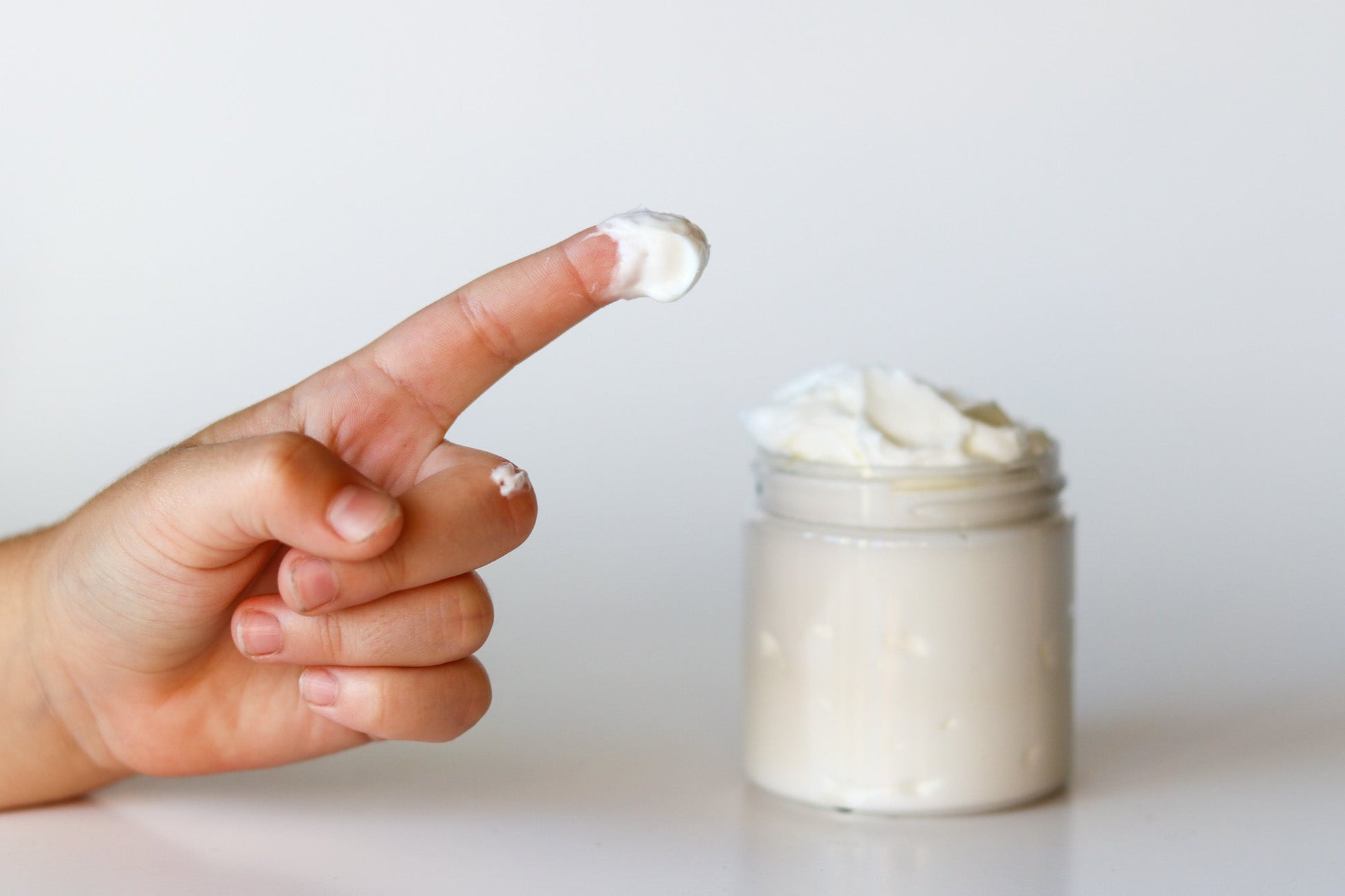 A dab of Sweetgrass Soap body butter on a fingertip beside the open jar, showing the soft texture.