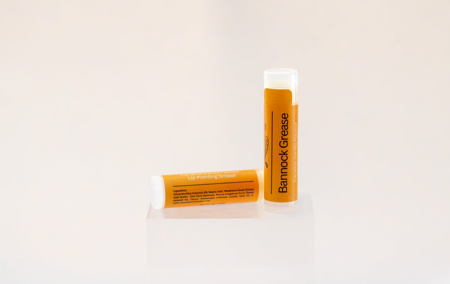 Sweetgrass Soap Bannock Grease lip balm twist-up tube with an orange caramel-vanilla label, two shown.