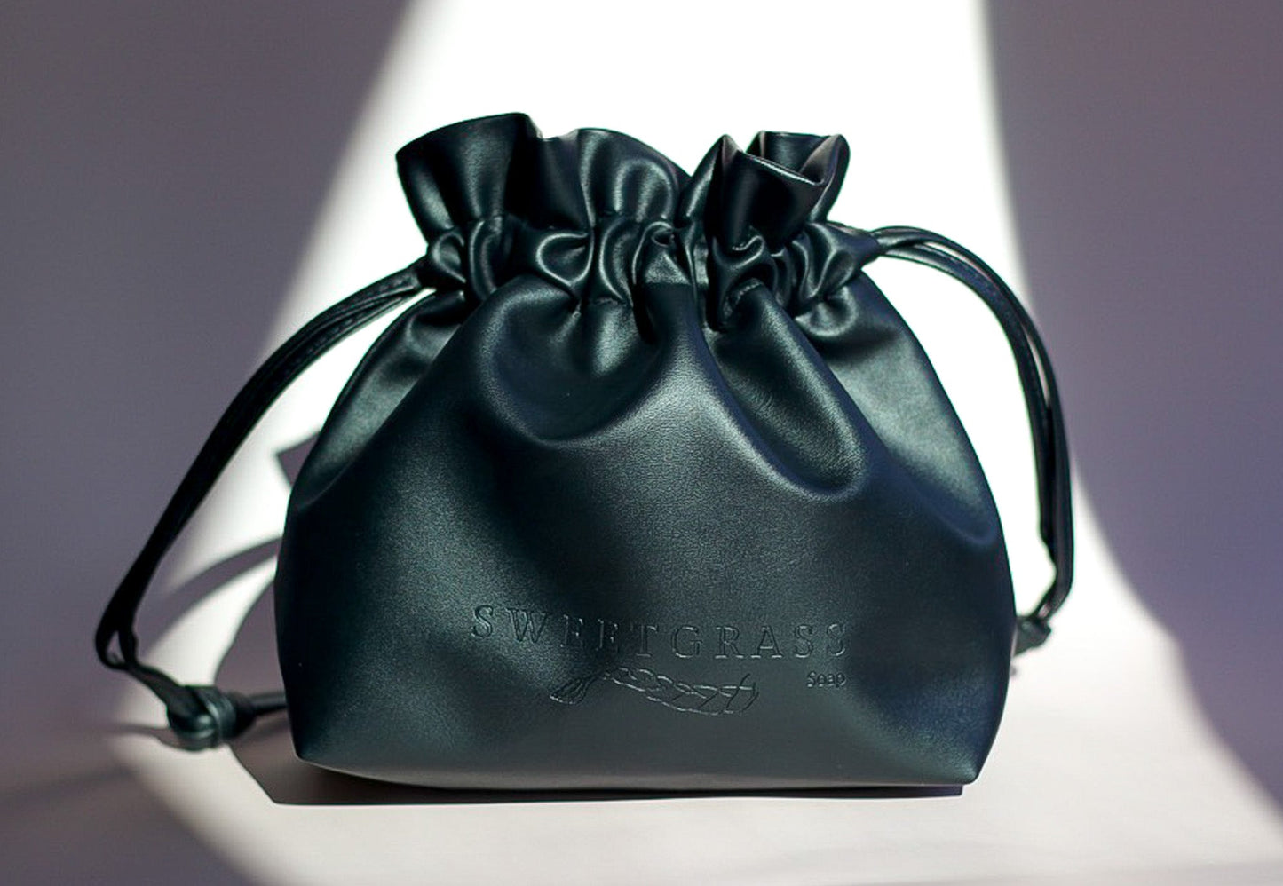 Sweetgrass Soap black vegan-leather drawstring toiletry bag with an embossed logo.