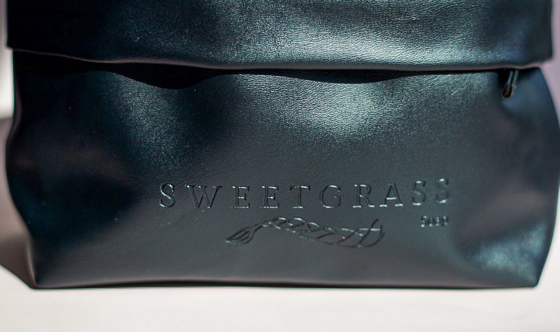 Close-up of the embossed Sweetgrass Soap logo on the black drawstring toiletry bag.