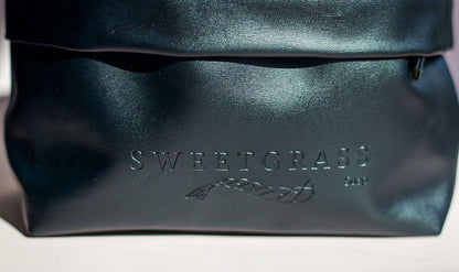 Close-up of the embossed Sweetgrass Soap logo on the black drawstring toiletry bag.