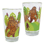 Set of two printed glass tumblers with a brown Sasquatch design among green trees by Francis Horne Sr.