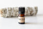 Sweetgrass Soap Smudge Oil Blend in a small 5 ml amber bottle with a black cap and kraft label, a sage bundle behind.
