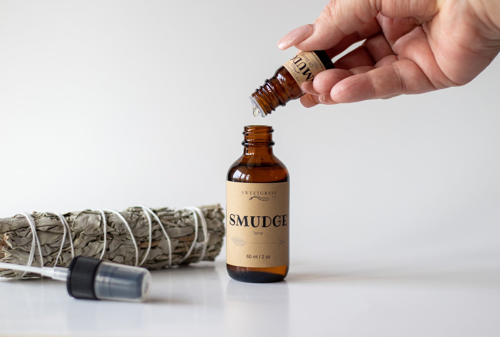Smudge Oil Blend being dripped into a Smudge Spray bottle to top it up, sage bundle beside.