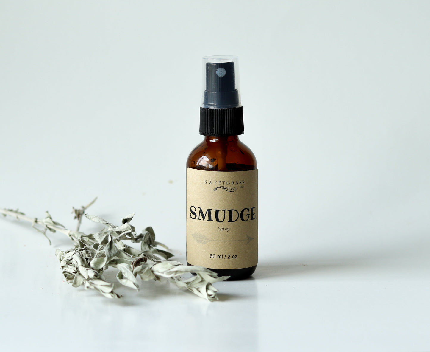Sweetgrass Soap Smudge Spray in a 2 oz amber glass bottle with a black mister and kraft label, dried sage beside it.