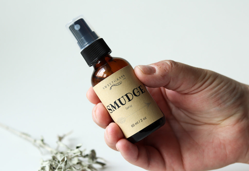 Hand holding the 2 oz Sweetgrass Soap Smudge Spray amber bottle, dried sage below.