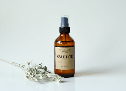 Sweetgrass Soap Smudge Spray in a 4 oz amber glass bottle with a black mister and kraft label, dried sage beside it.