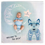 Baby in a blue onesie lying on a blanket with a wolf design and 'Welcome to the pack!' text.